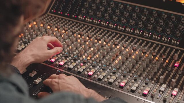 Over the shoulder slowmo of man adjusting sound on audio mixer while recording music at studio using professional equipment