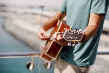 Close-up of a man playing a classical guitar while sitting on the beach in summer. Lifestyle, rest, relaxation