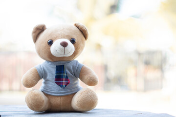 A brown teddy bear in a shirt and tie sits on a wooden background with a green background background. There is free space to insert a message.