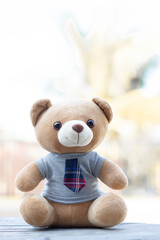 Vertical photo brown teddy bear in a shirt and tie sits on a wooden background with a green background background.