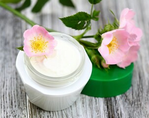 Obraz na płótnie Canvas Cosmetic cream with pink flower wild rose. Moisturizer cream with flowers on the white wooden table.