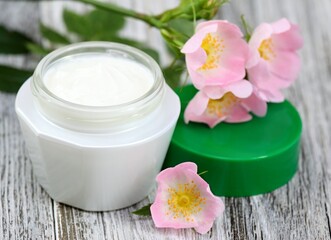 Fototapeta na wymiar Cosmetic cream with pink flower wild rose. Moisturizer cream with flowers on the white wooden table.