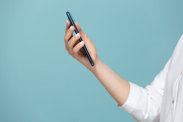 Close-up of a woman's hand with a smartphone on which there is a white screen for advertising, on a blue background. Copy paste.