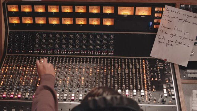 Top view slowmo of sound engineer operating mixing console while recording new track at studio with love song lyrics on mixing desk