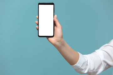 Close-up of a woman's hand with a smartphone on which there is a white screen for advertising, on a blue background. Copy paste.