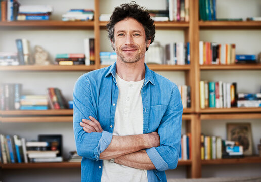 Hes a self-professed bibliophile. Shot of a happy bachelor posing with his arms crossed in front of a bookshelf at home.
