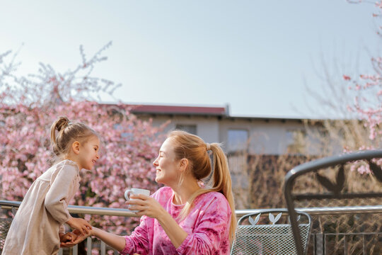 Banner Mom and daughter on the terrace at breakfast against the background of cherry blossoms in the morning