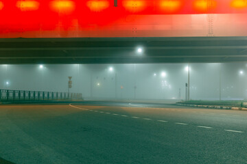 Fototapeta na wymiar View of a multi-lane road in the fog under the illuminated bridge. Foggy city road.