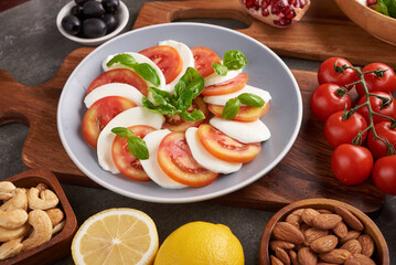 Italian caprese Salad with tomatoes, basil, mozzarella, olives and olive oil on wooden background. Italian traditional caprese salad ingredients. Mediterranean, organic and natural food concept.