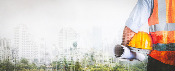 Double exposure of architect man holding helmet and project paper plan with abstract building city backgrounds, image panorama for cover design.