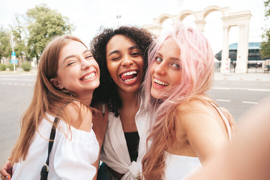 Three young beautiful smiling hipster female in trendy summer clothes.Sexy carefree multiracial women posing on the street background.Positive models having fun in sunglasses. Taking selfie photos
