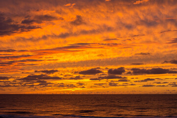Fototapeta na wymiar Yellow and orange sundown. The sundown over the ocean without sun. Orange and yellow cloudy evening sky