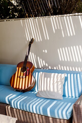 An acoustic guitar stands on a blue sofa next to a pillow on the terrace