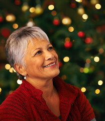 Christmas contemplation. Shot of a mature woman looking thoughtful in front of a Christmas tree.