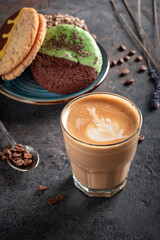 A glass of cappuccino or latte with foam and cookies on a dark stone background