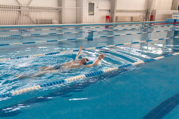 A male athlete swims in a swimming pool sports complex in blue water.