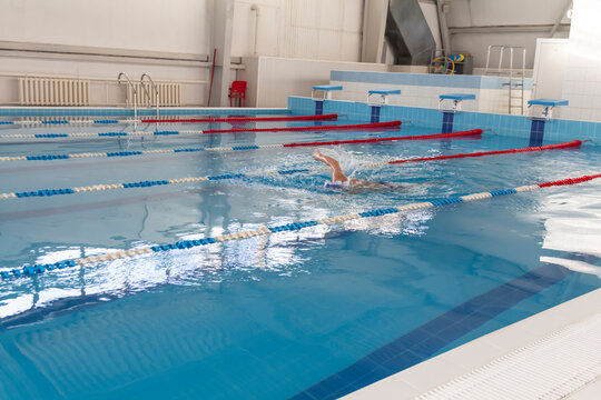 A male athlete swims in a swimming pool sports complex in blue water.