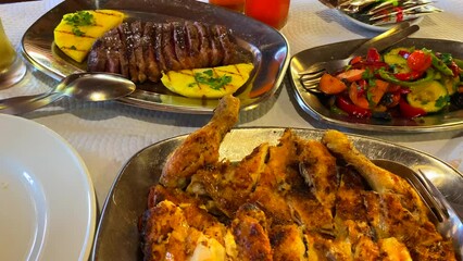 Delicious spicy piri piri chicken with fries, cooked vegetables and a picanha steak with pineapple, tasty traditional portuguese brazilian food in a restaurant, 4K shot