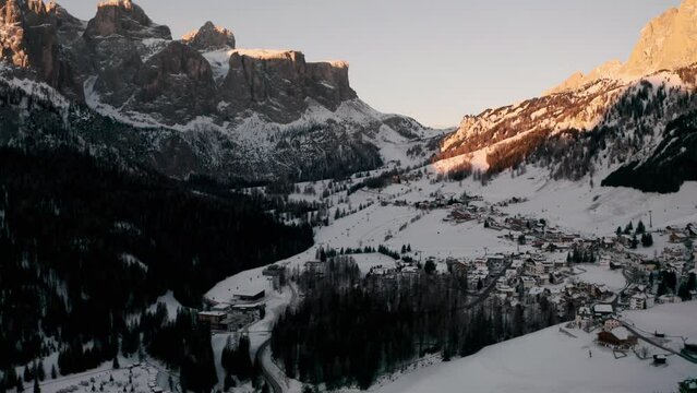Dolly back establishing drone shot over Colfosco mountain village in winter at sunrise