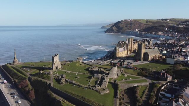 An aerial view of the the Welsh town of Aberystwyth showing the castle ruin and seafront. Flying right to left with slow zoom in over the town on a sunny spring morning, Ceredigion, Wales, UK.