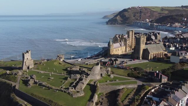 An aerial view of the the Welsh town of Aberystwyth showing the castle ruin and seafront. Flying left to right with slow zoom out over the town on a sunny spring morning, Ceredigion, Wales, UK.