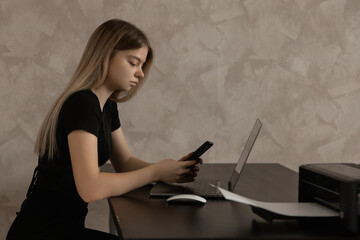 beautiful girl working remotely at home at the computer and typing a message on the phone