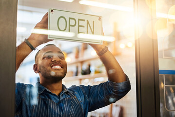 Our doors are now open. Shot of a young man hanging up an open sign in his store.