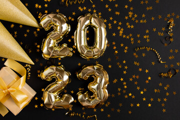 Golden foil balloons in the shape of figure 2023 on a black background. The concept of celebrating the new year.