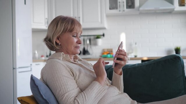 Housewife In Living Room Lying On Couch Uses Smartphone