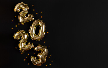 Golden foil balloons in the shape of figure 2023 on a black background. The concept of celebrating...