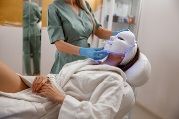 Woman getting cosmetic procedure with LED facial mask. Photon therapy.