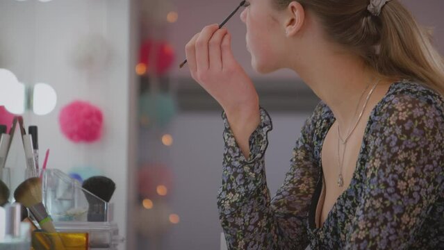 Teenage girl looking in mirror in bedroom at home putting on eye make up - shot in slow motion