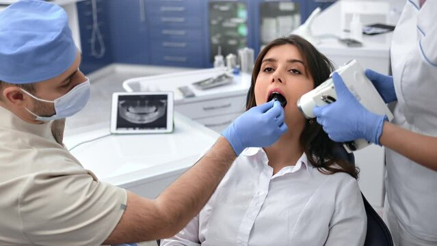Professional stomatologist male doctor and female assistant roentgen shooting mouth cavity patient 