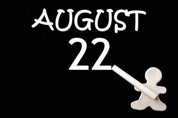 A small white plasticine man writing the date 22 August on a black board. Business concept. Education concept.