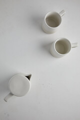 Big set of empty white ceramic plates and other tableware different size and shapes over white linen tablecloth. Flat lay