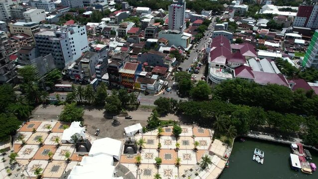 drone flying over a busy street in Makassar city Sulawesi Indonesia on a sunny day with large buildings and a river below.