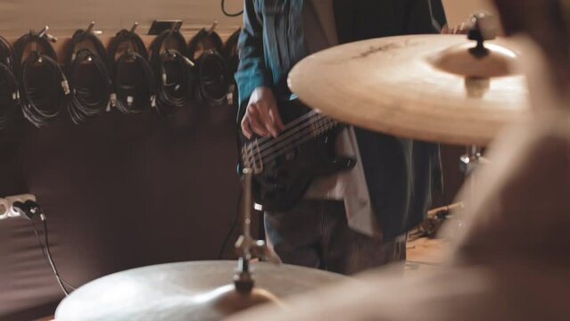 Midsection slowmo of emotional rock guitarist jumping and shaking his head while playing black bass guitar at music studio