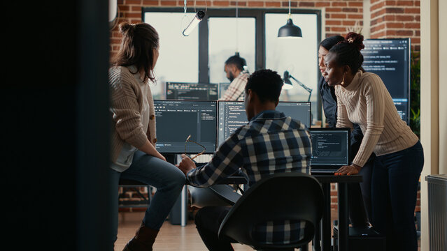 Software programmers discussing about online cloud computing while the rest of the team joins in front of multiple screens compiling code. Coders doing teamwork looking at running algorithms.