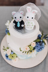 Decor. Wedding. White cake decorated with greenery and figurines of the bride and groom in the form of bunnies