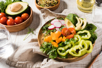 Vegetable summer salad with avocado, seasonal vegetables, spinach and micro-greens on a wooden white background. 