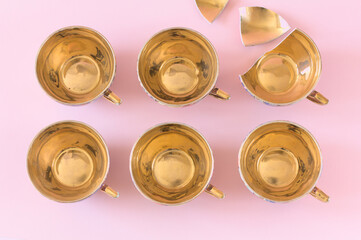 Vintage patterned teacups with a golden center on a pink background. One of them is broken. Top view, copy space.