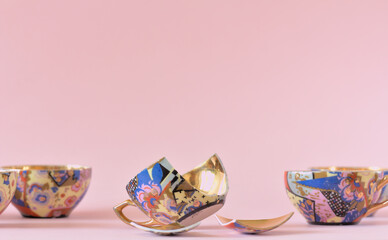 Vintage patterned teacups with a golden center on a pink background. One of them is broken. Copy space.