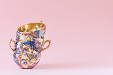 A stack of vintage, patterned teacups with golden center on a pink background. Copy space.