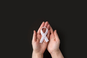 Concept lung cancer awareness. Women's hands hold white ribbon on black background. Bone cancer....