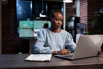 Forex stock market professional trader sitting at desk with laptop while buying and selling trading options. African american woman sitting in office workspace while analyzing real time financial data