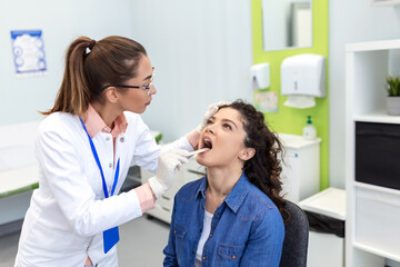 Doctor with depressor checking sore throat. Experienced doctor examines adult woman for sore throat