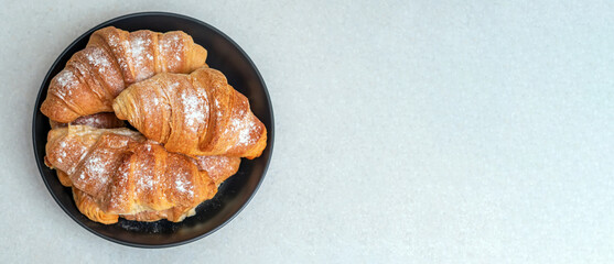 Homemade croissants on a dark plate sprinkled with powdered sugar. Flat lay