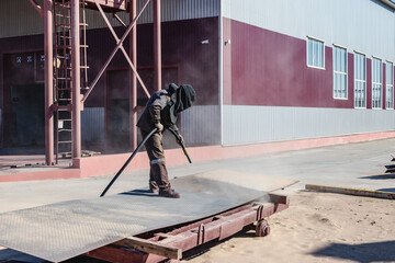 A worker in a special suit is sandblasting metal at an industrial site.