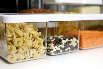 Transparent containers filled with pasta, legumes and cereals on the shelf in kitchen. Organization of storage of bulk food