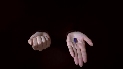 Red and blue pills on hands isolated on a black background. The Hand offering a blue pill